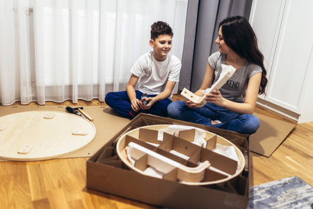 Brother and sister in casual clothing assembling furniture in apartmentの写真素材