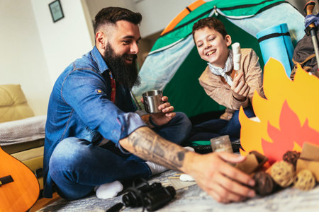 Dad with his son camp inside their home. They have pitched a tent and have a fake campfire.の写真素材