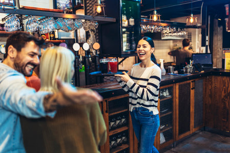 Young female waitress or bartender serving drinks in a bar carrying a tray with beerの写真素材