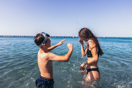 Brother and sister playing in the shore break on the beach during the hot summer vacation day.