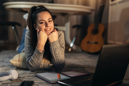 Happy teen girl learning on floor at home with books and laptop.