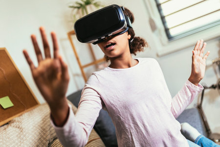 African American girl using virtual reality glasses in her room. Black girl enjoys VR technology to...