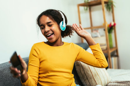 African American girl enjoying free time at home while sitting on the bed and listening to music...