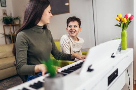 Brother and sister play electric piano at home and have fun. The sister helps her younger brother to play pianoの写真素材