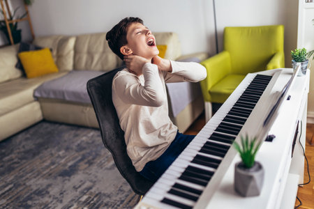 Little boy playing piano in living room. The boy is suffering from neck pain.の写真素材