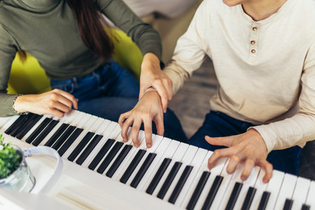 Brother and sister play electric piano at home and have fun. The sister helps her younger brother to play pianoの写真素材