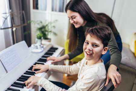 Brother and sister play electric piano at home and have fun. The sister helps her younger brother to play pianoの写真素材