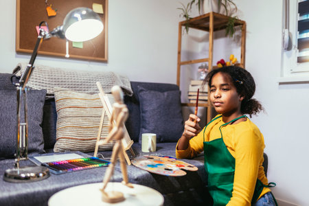Black preteen girl happily at a table, surrounded by an array of creative materials for painting to inspire their next great idea.の写真素材