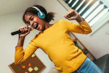 Cute preteen black girl  holding microphon singing karaoke at home, recording songs for contest. Children's lifestyle conceptの写真素材