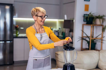 Senior woman in casual home clothes prepares healthy cocktails with different seasonal fruits.の写真素材
