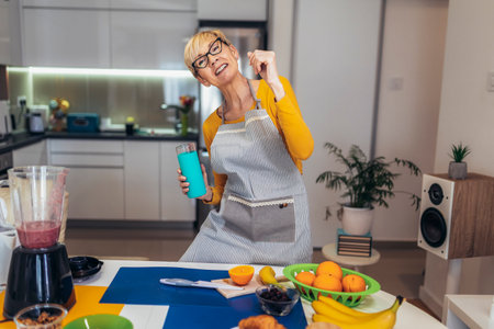Senior woman in casual home clothes prepares healthy cocktails with different seasonal fruits, drinking juice and having fun.の写真素材