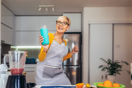 Senior woman in casual home clothes prepares healthy cocktails with different seasonal fruits, drinking juice and having fun.の写真素材