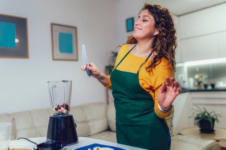 Beautiful, happy young woman in casual home clothes prepares fitness cocktails with different seasonal fruits.の写真素材