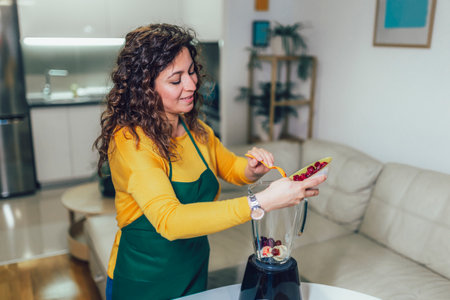 Beautiful, happy young woman in casual home clothes prepares fitness cocktails with different...