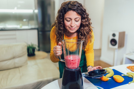 Beautiful, happy young woman in casual home clothes prepares fitness cocktails with different seasonal fruits.の写真素材