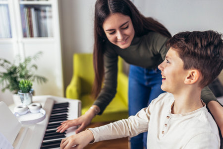 Brother and sister play electric piano at home and have fun. The sister helps her younger brother to play pianoの写真素材