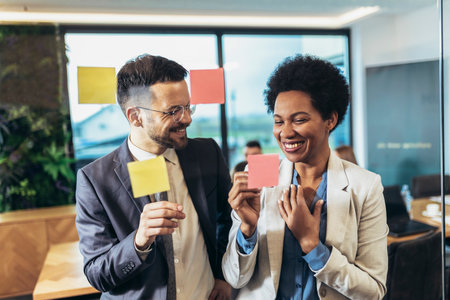 Young woman of a small company putting an adhesive note on glass in office during team meeting formulating business strategies.の写真素材