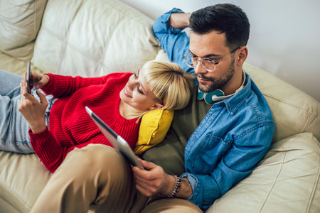 Beautiful couple hugging relaxing on sofa and using digital tablet and phone.の写真素材