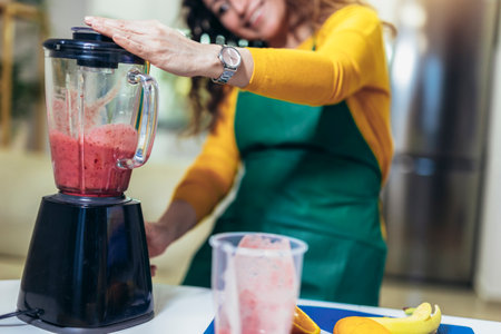 Beautiful, happy young woman in casual home clothes prepares fitness cocktails with different seasonal fruits.の写真素材