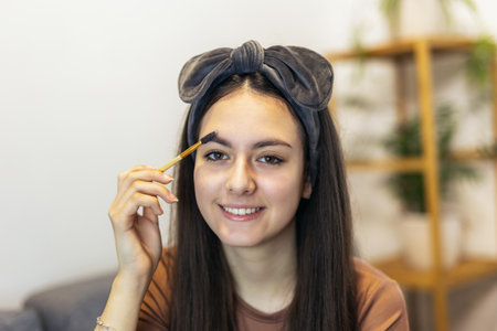 Cute teenage girl smile, make up face hand by applying mascara brush on eyebrows at home.の写真素材