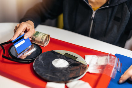 Senior woman drug addict making cocaine line with credit card on glass surface.