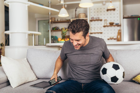 Young soccer fan man watching football game on television at living room couch.の写真素材