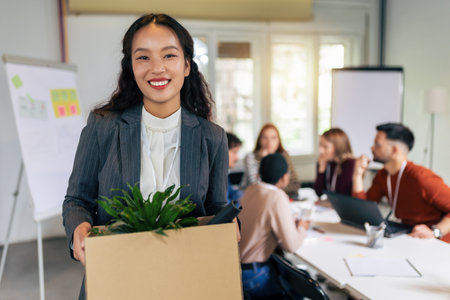 Business team meets a new employee.  New coworker holding a box standing in the modern office with other colleaguesの写真素材