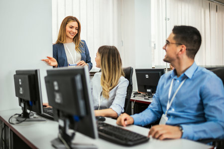 A group of students each sit in front of a desktop in a computer lab. They are each focused on their...