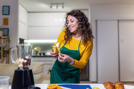 Beautiful, happy young woman in casual home clothes prepares fitness cocktails with different seasonal fruits.の写真素材