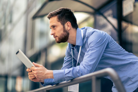 A serious businessman is outside of his job and he is using a tablet to work from it.の写真素材
