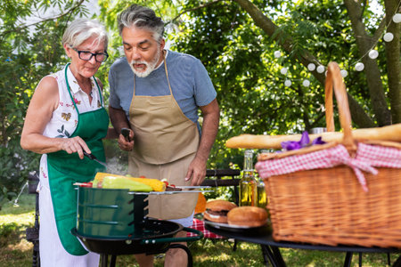 Elderly couple celebrate the 4th of July in their backyard. They are making barbeque, vegetables, and drinking beverages while enjoying and making memoriesの写真素材