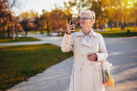 An older woman walking in the park and taking pictures of it with her groceries in the autumn