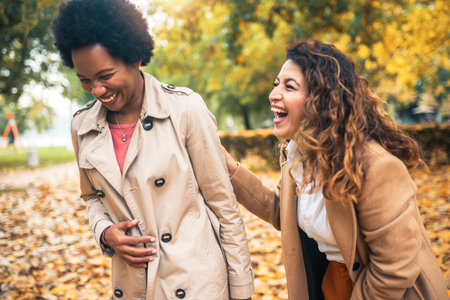 Happy woman friends walking in the forest in autumn. They are chatting and having fun.の写真素材