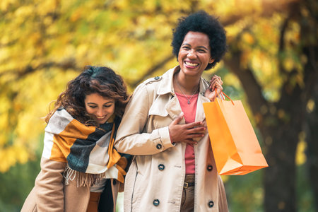 Happy woman friends walking in the forest in autumn with shopping bags.の写真素材