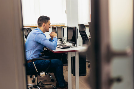 Young handsome businessman working and smiling at his computer in his office