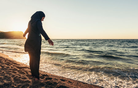 A woman in hijab standing on the beach looking at the horizonの写真素材