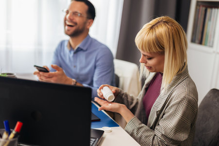 Woman sitting by the desk in the office and taking medical pills