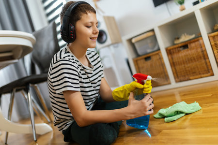 Male kid cleaning the floor with cloth while wearing the headphones and listening to the music