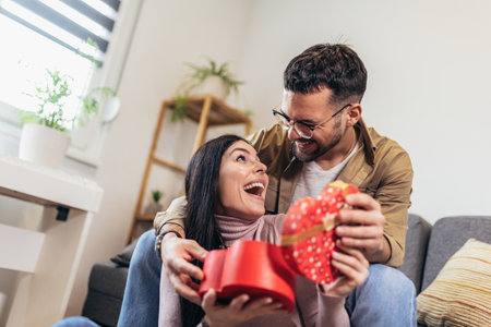 Man giving a surprise gift to woman at home. Party at home, birthday gift, anniversary, Valentines day and holidayの写真素材