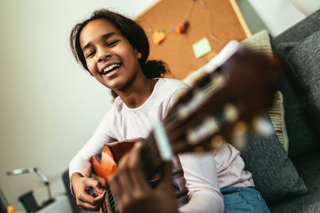 African american teenage girl sitting on couch in her room and learning to play guitar
