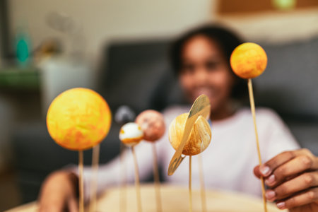 Happy african american school girl making a solar system for a school science project at homeの写真素材