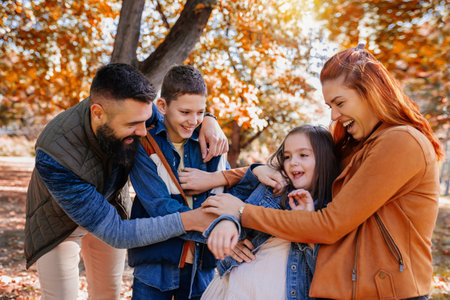 Parents tickle their children. Sunny autumn day in the colorful parkの写真素材