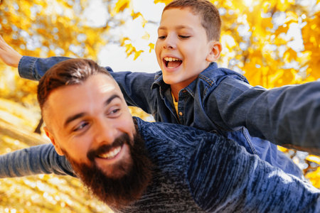 Father carries a son on his back. Having fun time in the colorful park on the sunny autumn day.の写真素材