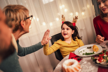 Grandmother and her granddaughter high five while the rest of the family is enjoying the Christmas dinner. Happy multi-generation familyの写真素材