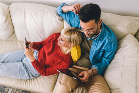 Beautiful couple hugging relaxing on sofa and using digital tablet and phone.の写真素材