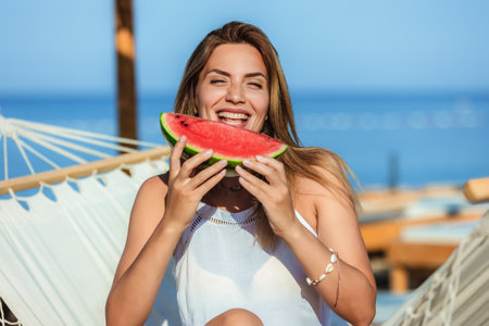 Young beautiful woman eating juicy watermelon on the beach.の写真素材