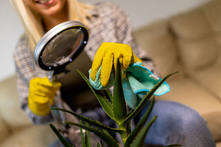 Young blonde woman taking care of her plants. Using magnifying glass