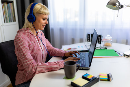Young blonde woman smiling while working on her laptop and drinking coffee