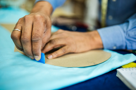 Young African American tailor drawing with chalk on material in his own atelier.
