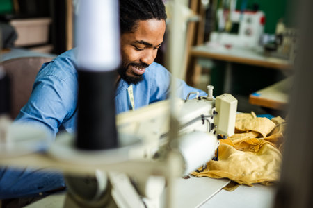 Young male African American tailor sew with a sewing machine in his own atelierの写真素材